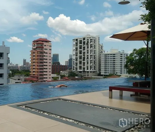 公寓 出租在Khlong Toei, Bangkok - 屋顶无边际泳池，可观城市天际线，设遮阳伞与座椅。