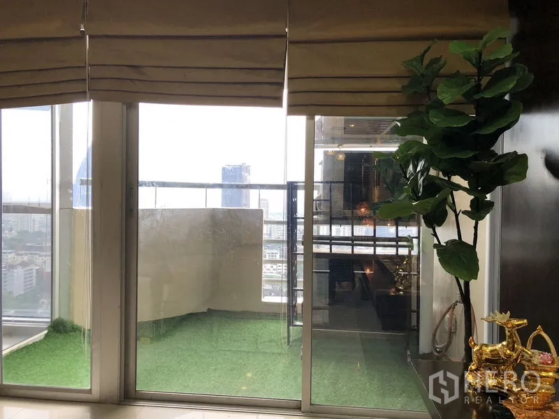 Condominium for rent in Khlong Toei, Bangkok - Balcony with artificial grass flooring and skyline view through glass doors.