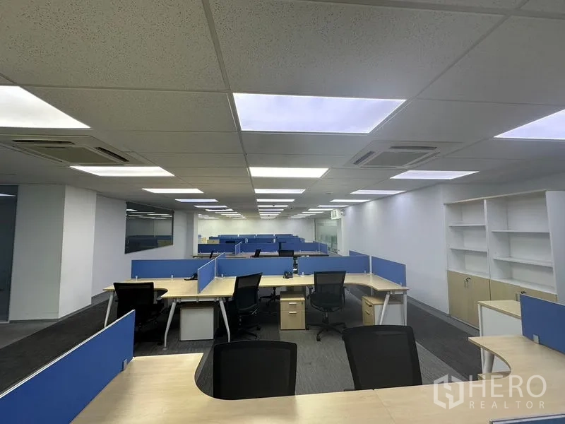 Office Space for rent - Collaborative open office area with L-shaped desks, blue dividers and wall shelving for storage.