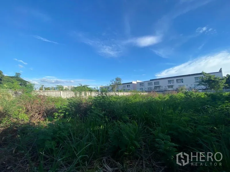Warehouse for rent in Suan Luang, Bangkok - Vegetation-filled open land within the compound with neighboring townhomes beyond the boundary wall.