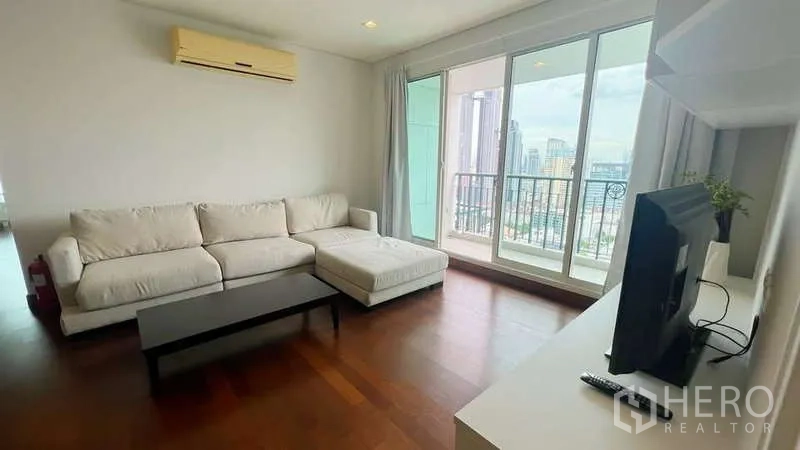 คอนโด ให้เช่าในWatthana, Bangkok - ผนังทีวีในห้องนั่งเล่น โซฟาสีขาว และประตูกระจกสู่ระเบียงวิวเมือง