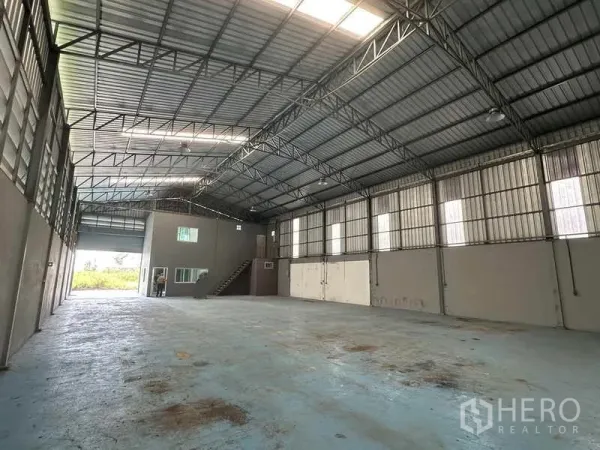 Warehouse for rent in Pathum Thani - Large open-plan storage area with ridge skylights, roller door access and side windows.