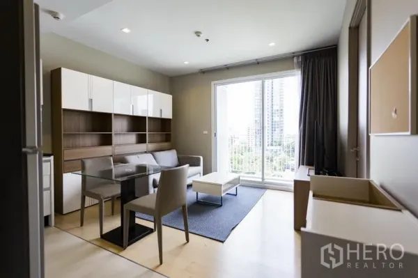 Condominium for rent in Watthana, Bangkok - Bright lounge with glass dining table and sliding doors to a balcony with city view.