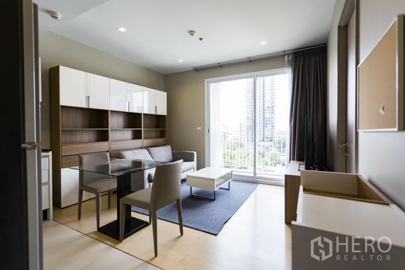 Condominium for rent in Watthana, Bangkok - Bright lounge with glass dining table and sliding doors to a balcony with city view.