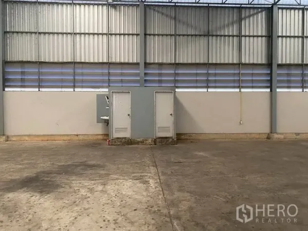 货栈 出租在Lat Krabang, Bangkok - 仓库墙面带通风百叶、两扇设备间门与洗手池，地面为混凝土