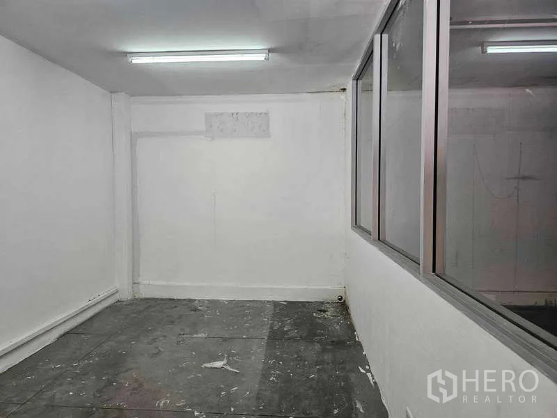 Warehouse for rent or sale in Khlong Toei, Bangkok - Compact office or storage room with fluorescent lighting beside a glazed partition wall.