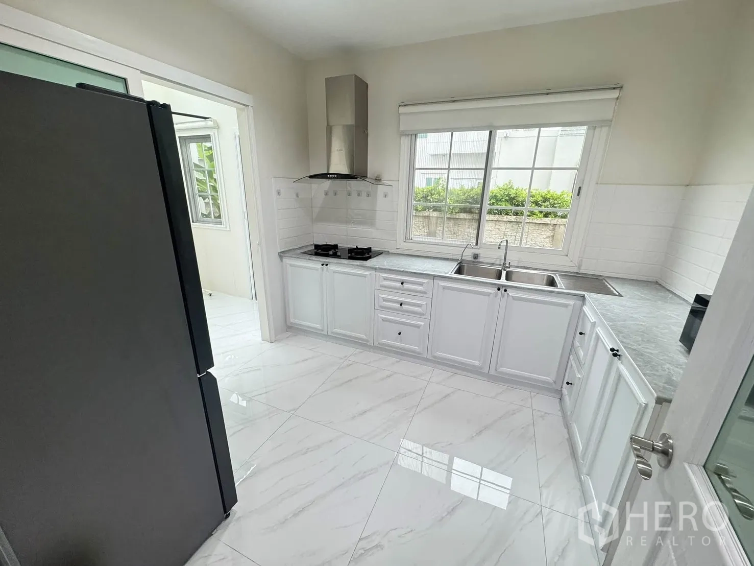 Detached House for rent or sale in Bang Phli, Samut Prakan - Bright U-shaped kitchen with gas hob, range hood, white cabinets, double sink and window.