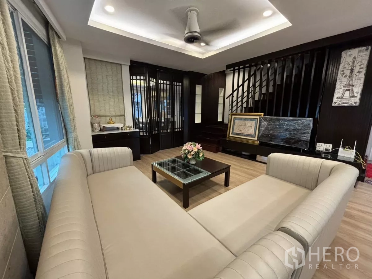 独立式住宅 出租在Bang Kapi, Bangkok - 温馨起居室，米色沙发、楼梯与深色木饰面。