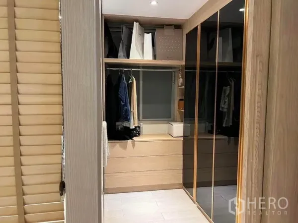 Condominium for sale in Huai Khwang, Bangkok - Walk-in closet with wood cabinetry, mirrored wardrobe doors, drawers and a small window under recessed lighting.