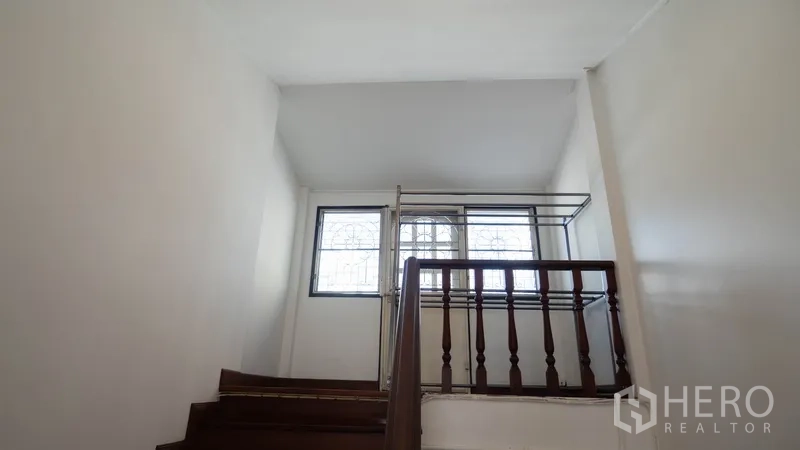 Townhouse for rent in Watthana, Bangkok - Stair landing with wooden railing and natural light from the window.