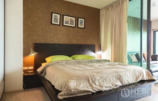 Condominium for rent in Khlong Toei, Bangkok - Cozy bedroom with a platform bed, bedside lamps, and a sliding glass partition.