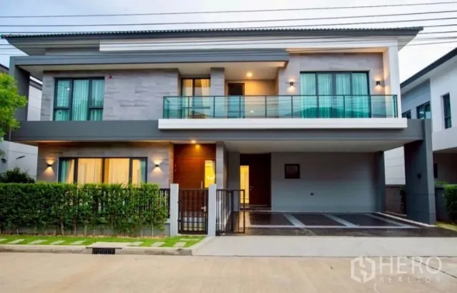 独立式住宅 出租在Bang Phli, Samut Prakan - 现代两层独栋别墅正立面，带阳台、暖色灯光与遮顶车位。