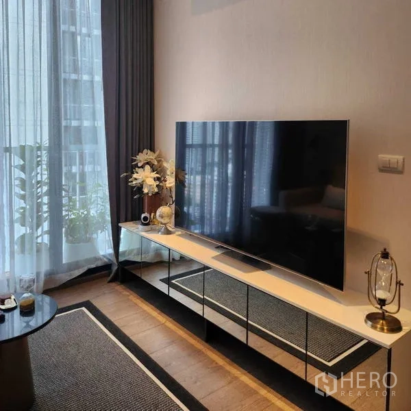 Condominium for rent - Large flat‑screen TV on a sleek console beside tall windows with sheer curtains.