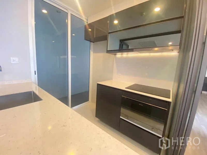 Condominium for rent in Bang Rak, Bangkok - Compact kitchen zone with glossy cabinets, cooktop and built-in oven under strip lighting.
