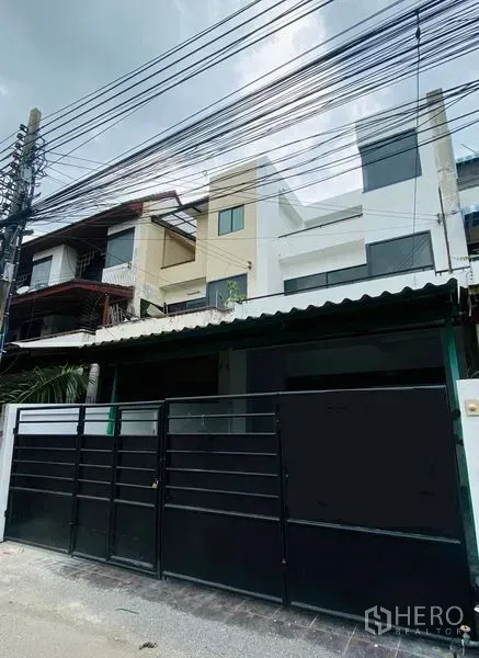 带办公室的家 出租或出售在Suan Luang, Bangkok - 街景外观，三层家办配黑色金属大门与空中电缆。