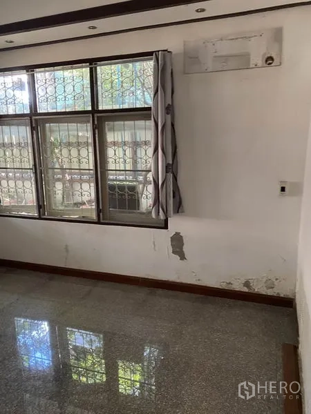 Townhouse for rent in Lat Phrao, Bangkok - Bright corner with large windows and metal security bars, showing worn paint on the wall.