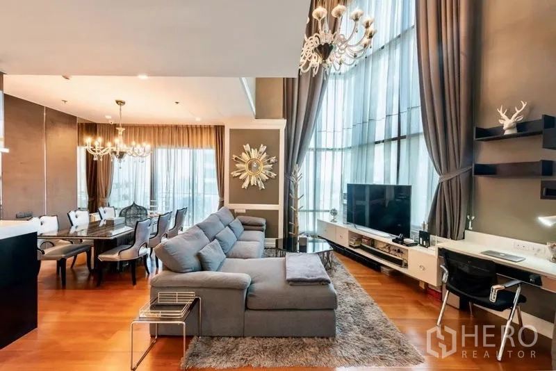 Condominium for rent in Khlong Toei, Bangkok - Elegant lounge with TV wall, work desk, chandeliers, and floor-to-ceiling drapes.