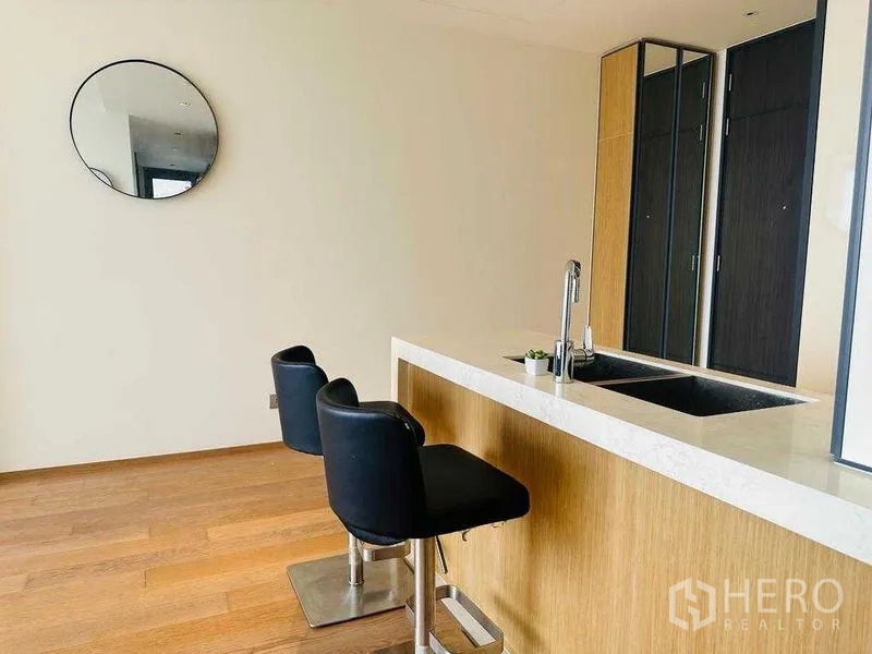 Condominium for rent in Khlong Toei, Bangkok - Breakfast bar kitchen with white countertop, sink, and two black stools.