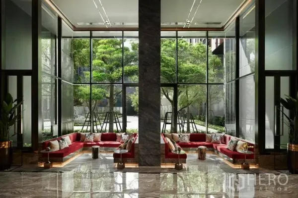 公寓 出售在Ratchathewi, Bangkok - 挑高大堂，落地窗与红色沙发，窗外绿树成景。
