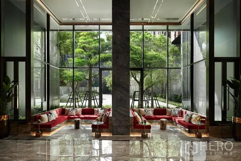 公寓 出售在Ratchathewi, Bangkok - 挑高大堂，落地窗与红色沙发，窗外绿树成景。