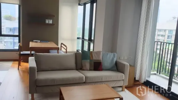 Condominium for rent in Phaya Thai, Bangkok - Corner living area with beige sofa, coffee table, floor-to-ceiling windows and a balcony overlooking Phaya Thai.