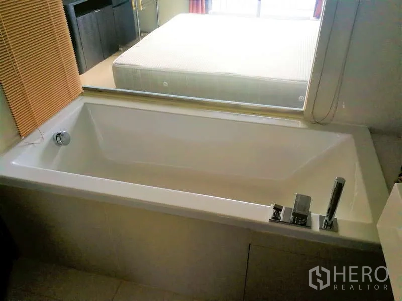 Condominium for sale - Rectangular white bathtub with mixer tap next to the bedroom window with blinds.