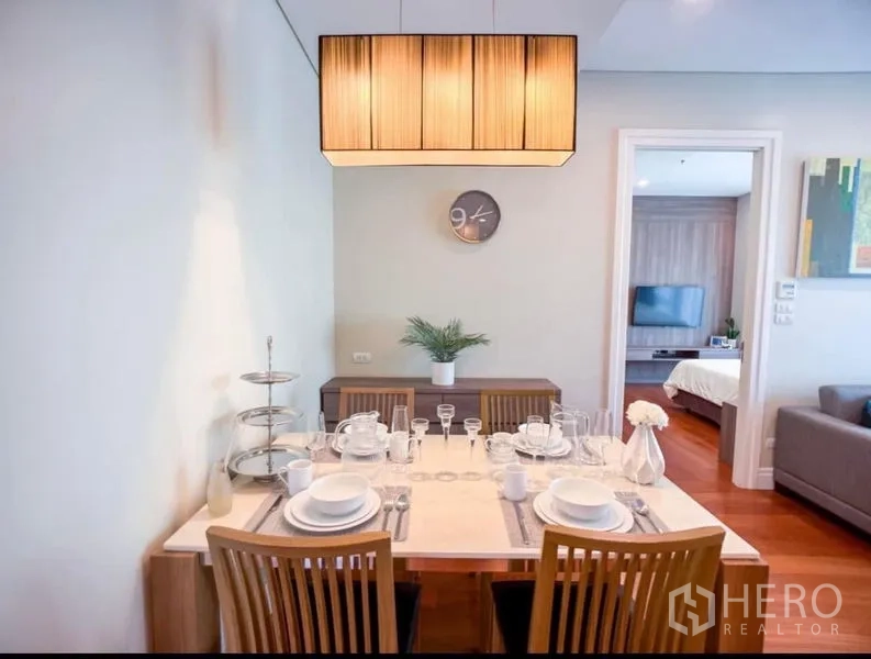 Condominium for rent in Khlong Toei, Bangkok - Dining area set for four beneath a warm pendant light with a doorway to the bedroom.
