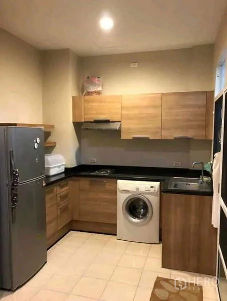 Townhouse for rent in Phra Khanong, Bangkok - Compact Western kitchen with wooden cabinetry, black countertops, fridge and washing machine.
