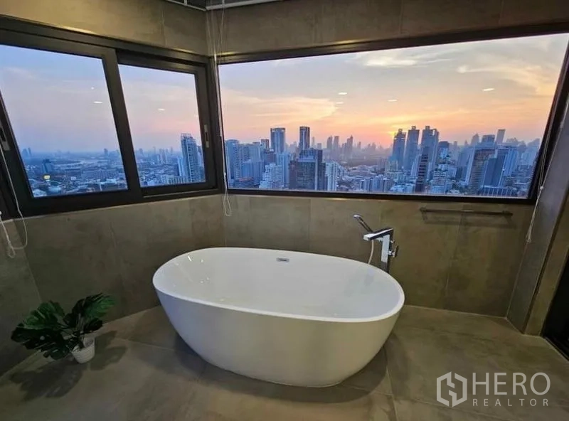 Condominium for rent or sale - Freestanding bathtub facing a panoramic Bangkok skyline at sunset.
