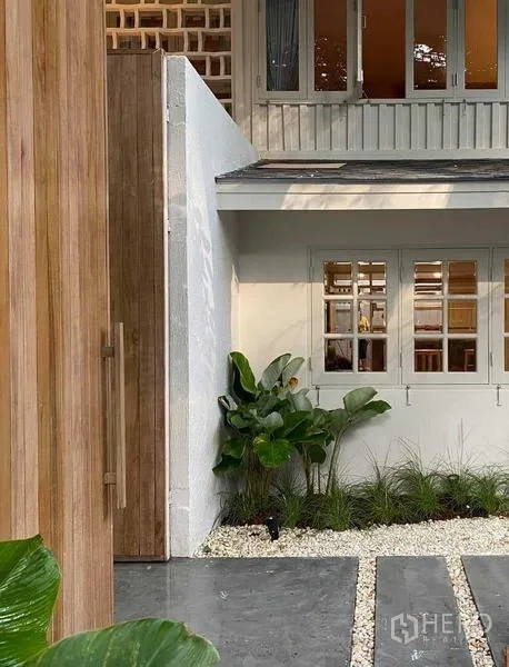 Detached House for rent in Watthana, Bangkok - Close-up of wooden entrance door and white windows with greenery.