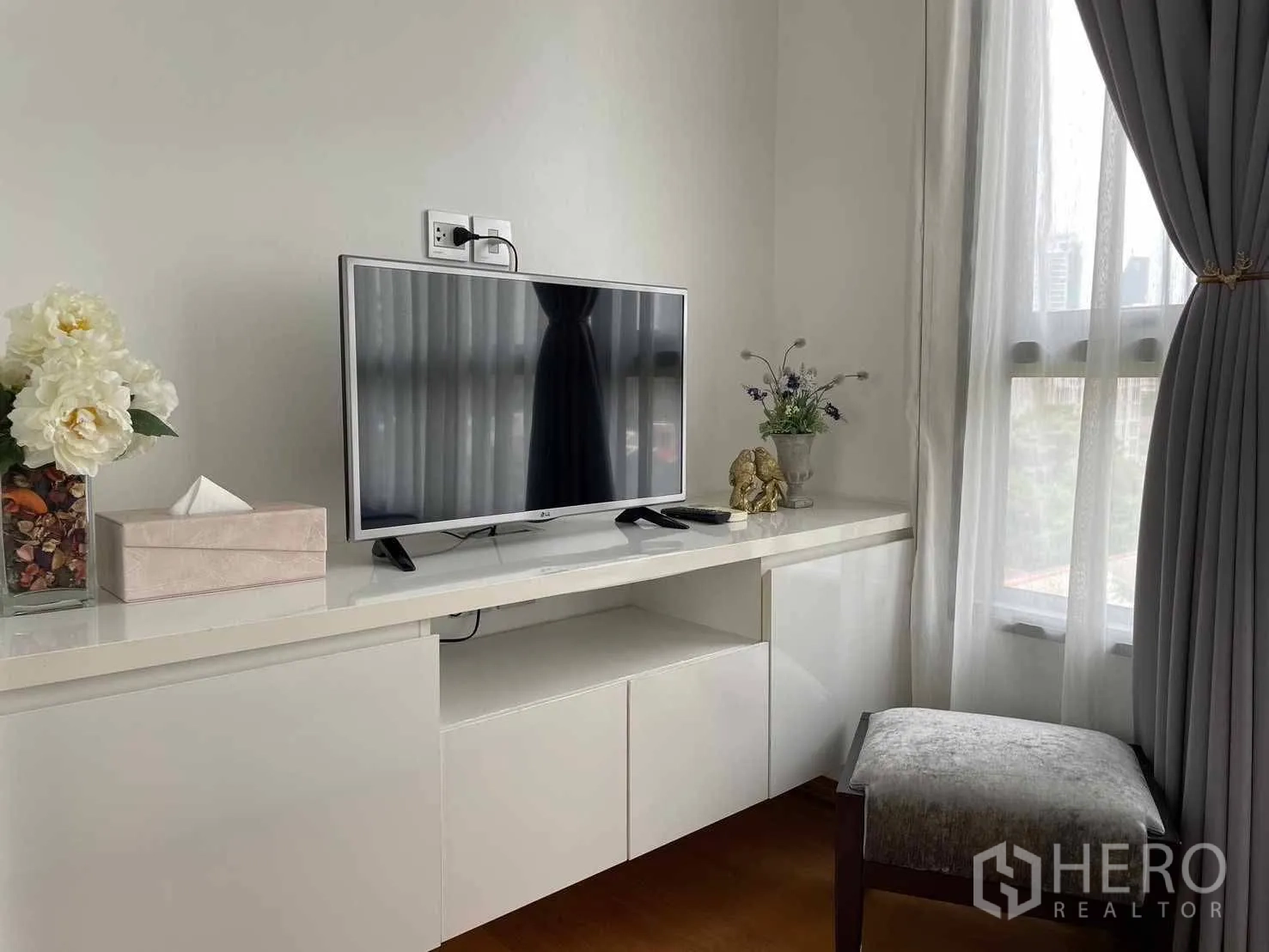 Condominium for rent in Watthana, Bangkok - Built-in white TV console with flat-screen television beside a sheer-curtained window.