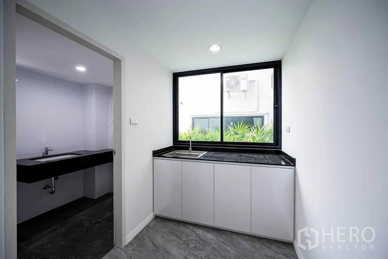 带办公室的家 出租在Suan Luang, Bangkok - 带黑色台面的紧凑茶水间和窗户，一侧有通往卫生间的门。