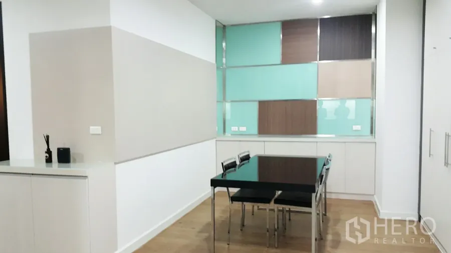 Condominium for rent in Khlong Toei, Bangkok - Bright dining area with a glass-top table, wood floors, built-in cabinetry and a colorful feature wall in a modern condo.