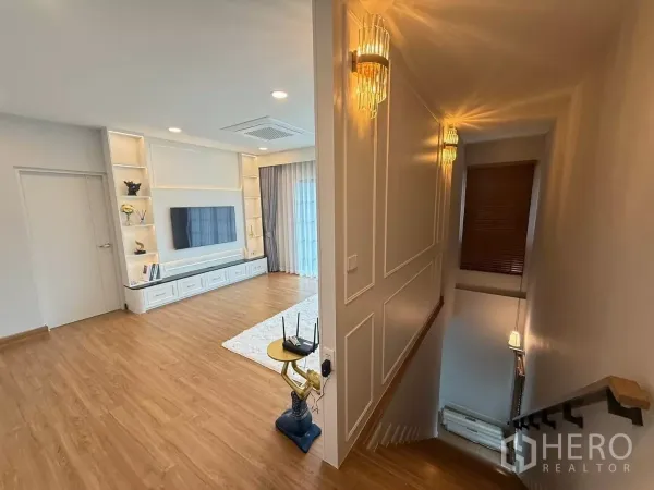 Detached House for rent in Bang Phli, Samut Prakan - Stair landing leading to an upstairs family room with wood flooring, TV wall and built-in shelving.