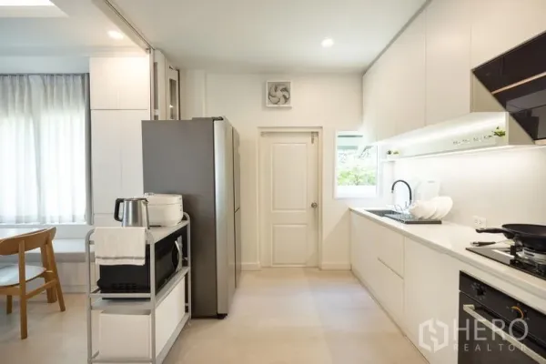 Detached House for rent or sale in Bang Phli, Samut Prakan - Modern white kitchen with built-in cabinets, gas stove, sink and large fridge.