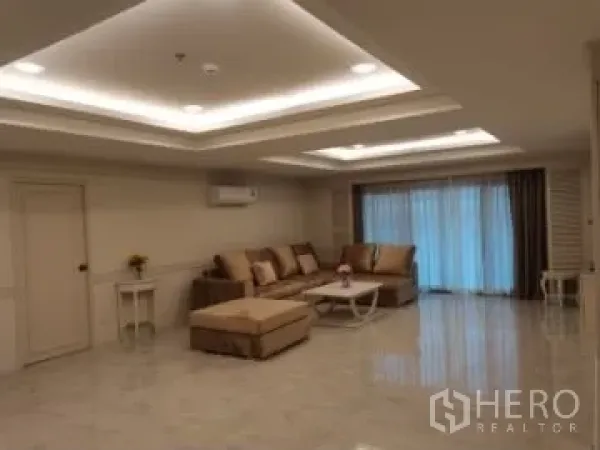 Apartment for rent in Watthana, Bangkok - Spacious living room with recessed ceiling lights, beige sectional sofa, shiny floor and sliding doors with curtains.