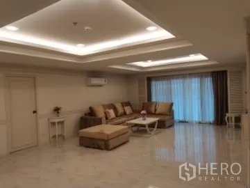 Apartment for rent in Watthana, Bangkok - Spacious living room with recessed ceiling lights, beige sectional sofa, shiny floor and sliding doors with curtains.