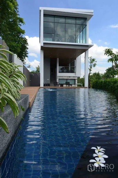 Detached House for rent or sale in Prawet, Bangkok - Communal swimming pool with a glass-walled clubhouse in the estate.