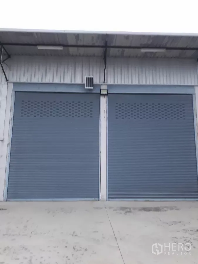 Warehouse for sale in Bang Len, Nakhon Pathom - Close-up of two large metal roller shutter loading doors under a canopy.