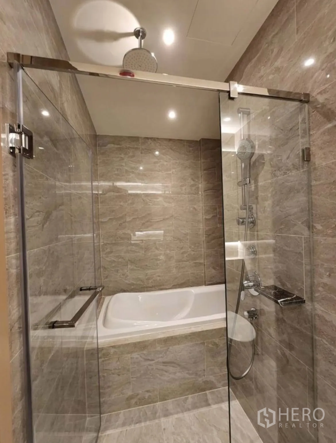 Condominium for rent in Din Daeng, Bangkok - Bathroom with glass-enclosed shower and bathtub finished in stone-look tiles.
