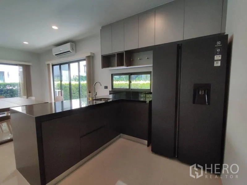 Detached House for rent in Bang Kapi, Bangkok - Sleek open kitchen with black stone peninsula, double-door refrigerator and ample storage.