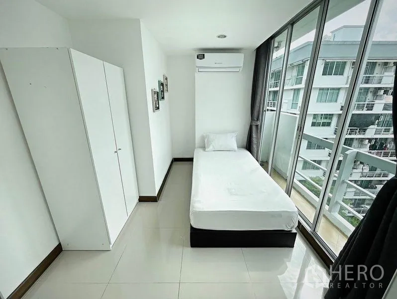 Condominium for rent in Khlong Toei, Bangkok - Compact third bedroom with single bed, wardrobe and wall-to-wall windows overlooking the city.