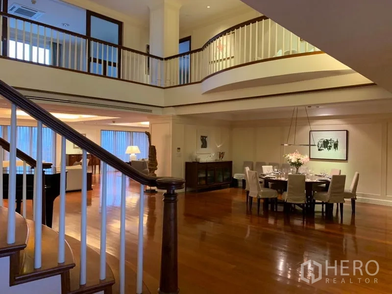 Condominium for rent or sale in Watthana, Bangkok - Double-height living and dining area with curved staircase and mezzanine in a luxury Watthana Bangkok condo.