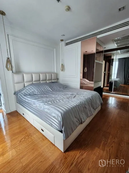 Condominium for rent in Bang Rak, Bangkok - Primary bedroom with upholstered headboard, pendant bedside lights, mirrored wardrobe and wood floors.