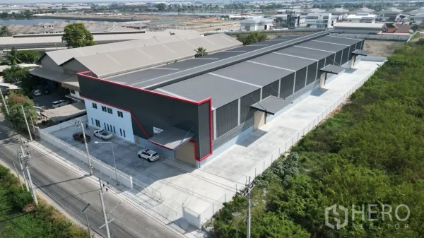 Warehouse for rent in Mueang Samut Prakan, Samut Prakan - Aerial view of a newly built grey warehouse with red trim, large concrete yard and attached office block in Samut Prakan.