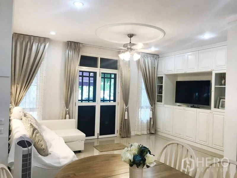 Townhouse for rent in Phra Khanong, Bangkok - Living room with white built-in TV wall and sectional sofa.