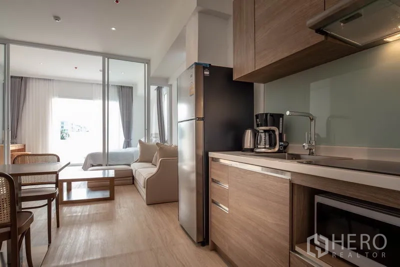Condominium for rent in Khlong Toei, Bangkok - Compact kitchen with wood cabinets, dining set and sliding glass doors connecting to the bedroom.