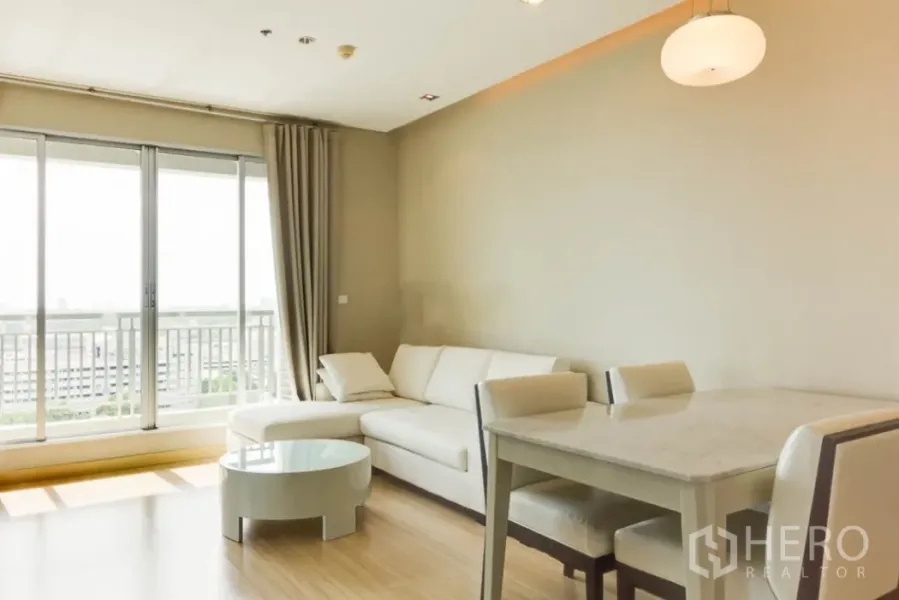 คอนโด ให้เช่าในRatchathewi, Bangkok - ห้องนั่งเล่นสว่าง โซฟาเข้ามุมสีขาว กระจกบานเลื่อนสูงจรดเพดาน และระเบียงวิวเมือง