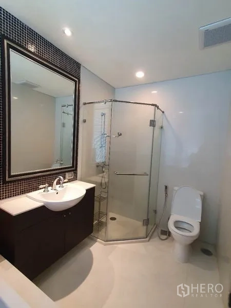 公寓 出租在Khlong San, Bangkok - 卫浴间，玻璃淋浴房、带大镜子的洗手台与坐便器。