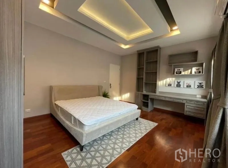 Detached House for rent or sale in Bang Phli, Samut Prakan - Guest bedroom featuring bed, built-in desk and shelves, wooden floor and warm ceiling lights.